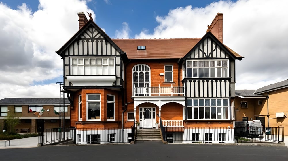 Das Tudor-Gebäude der Sandford Park School zeigt eine detailreiche Backstein- und Fachwerkfassade mit Bogenfenstern unter blauem Himmel.