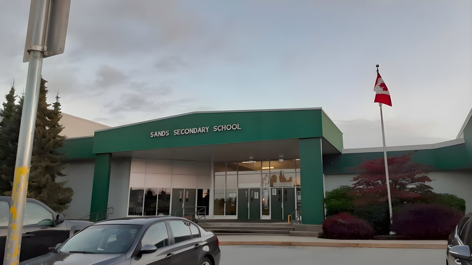 Das grün gestrichene Schulgebäude der Sands Secondary School mit einer kanadischen Flagge und Bäumen im Umfeld.