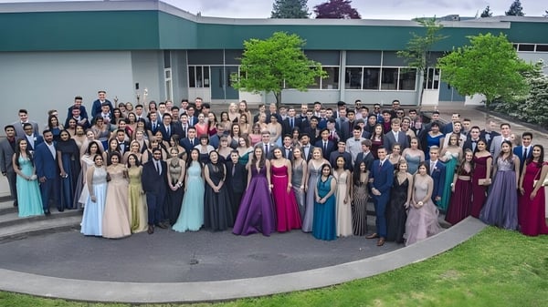Eine große Gruppe Schüler in formeller Kleidung steht vor dem grünen Gebäude der Sands Secondary School.
