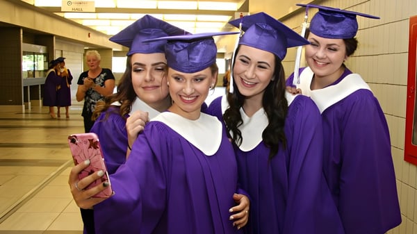 Schülerinnen der Sandwich Secondary School posieren in lila Abschlussroben für ein Selfie im Flur.