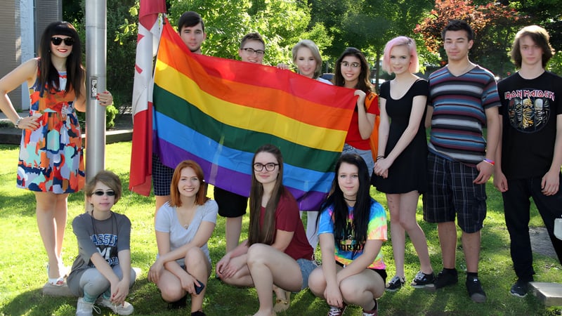 Eine Gruppe von Schülerinnen und Schülern der Sandwich Secondary School posiert draußen mit einer Regenbogenflagge in einem parkähnlichen Umfeld.
