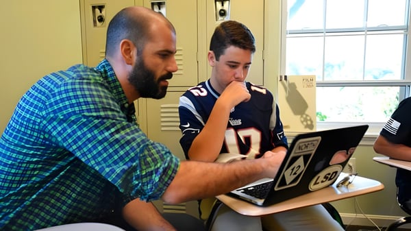Ein Mann mit Bart und ein Schüler sitzen gemeinsam am Laptop auf dem Campus der Sandy Spring Friends School.
