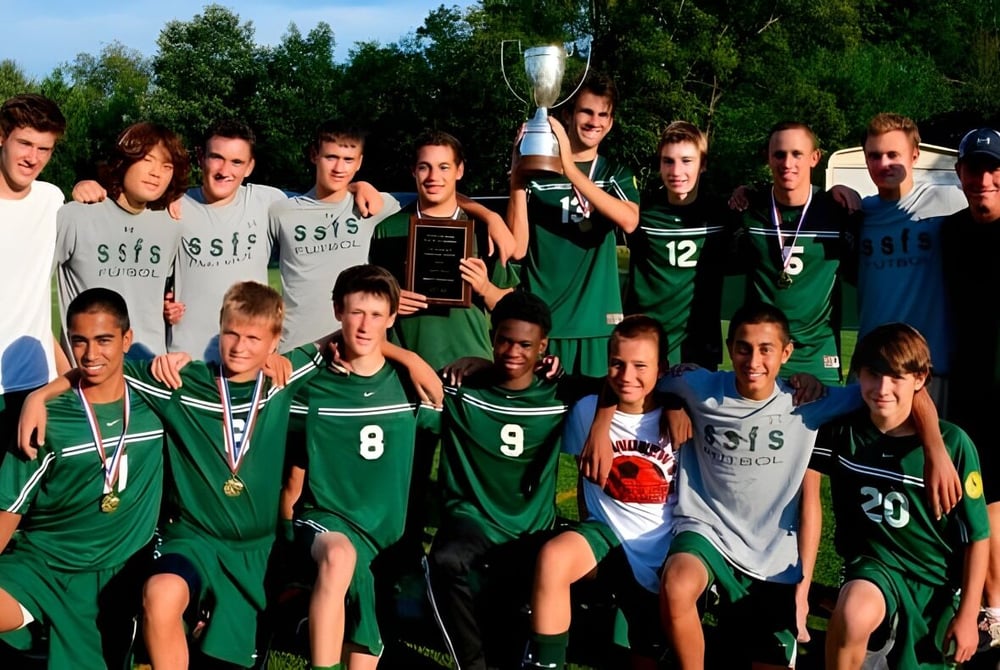 Schüler der Sandy Spring Friends School feiern auf dem Sportfeld ihren Sieg mit einem Pokal in der Hand.