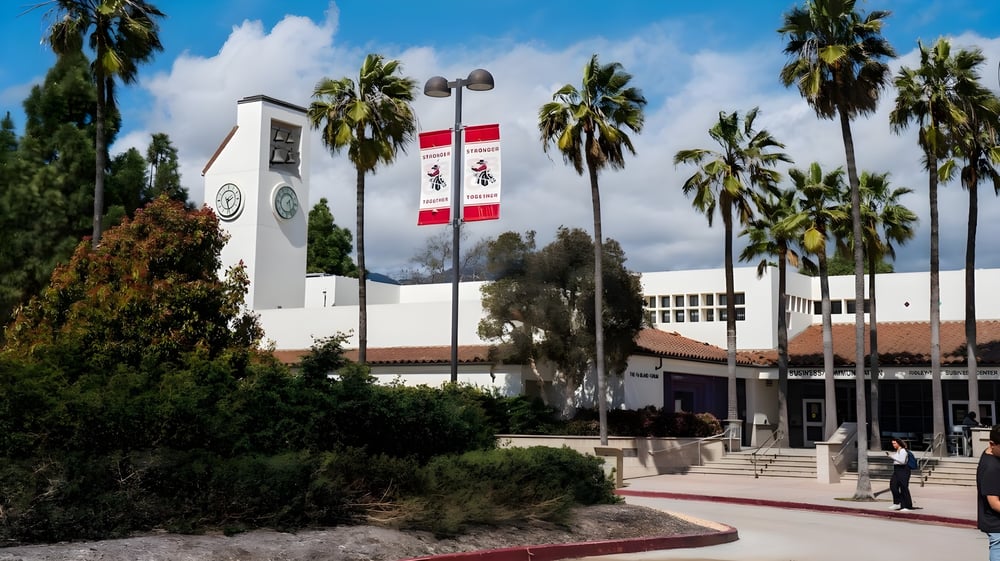 Das weiße Hauptgebäude mit Uhrturm auf dem Campus des Santa Barbara City College ist von Palmen und einem Weg umgeben.