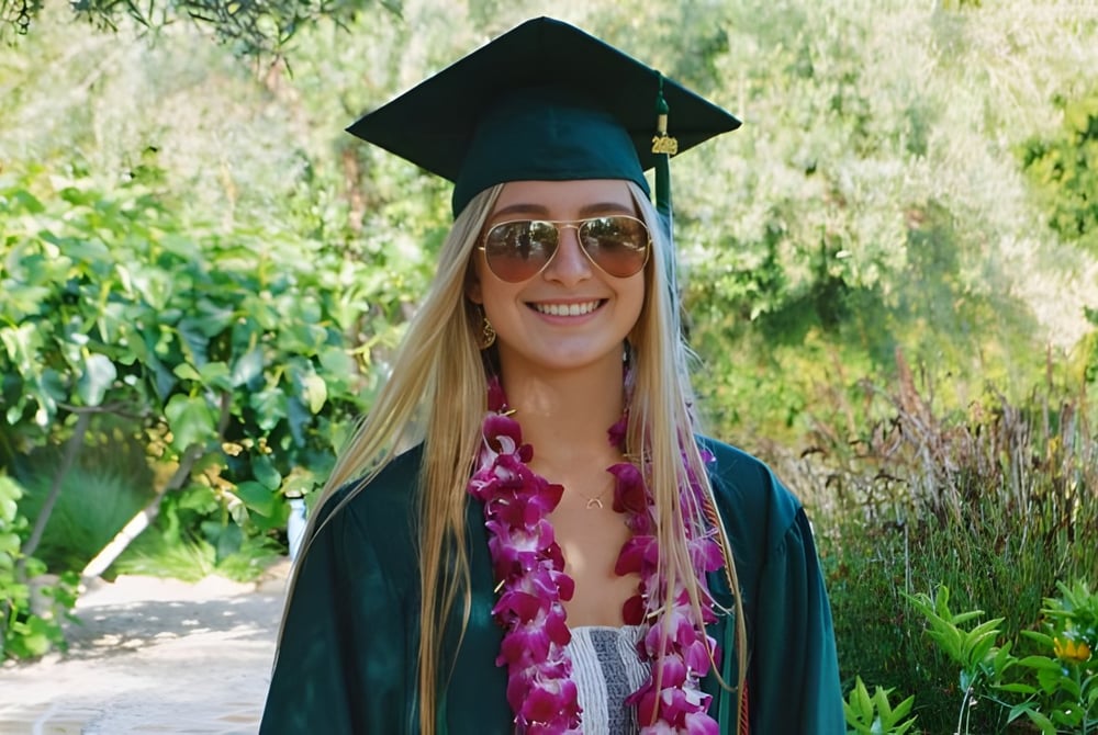 Eine junge Frau in Abschlusskleidung steht im Grünen auf dem Campus des Santa Barbara Unified School District.