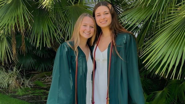 Zwei Schülerinnen stehen zusammen in einer tropischen Umgebung mit großen Palmenblättern auf dem Gelände des Santa Barbara Unified School District.