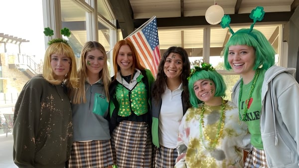 Eine Gruppe von Frauen in festlicher Kleidung posiert vor einer amerikanischen Flagge auf dem Campus der Santa Catalina School.