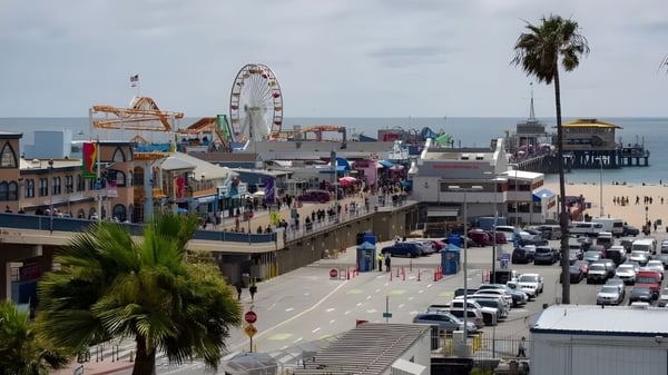 Schüler des Santa Monica College gehen entlang des belebten Boardwalks mit Riesenrad und Freizeitparkattraktionen am Meer.