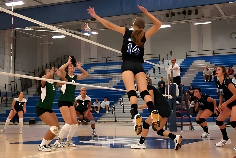 Weibliche Volleyballspielerinnen vom Santa Monica College spielen aktiv ein Volleyballspiel mit einem Spike über das Netz.