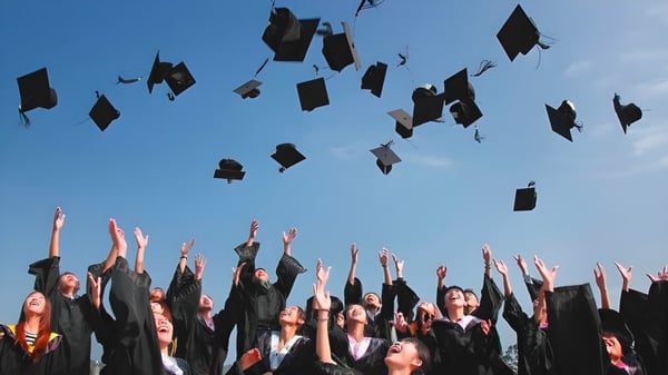 Absolventinnen und Absolventen der Sardis Secondary School werfen während der Abschlussfeier ihre Hüte in den blauen Himmel.