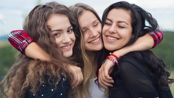 Drei Schülerinnen der Sardis Secondary School umarmen sich lachend im Freien.