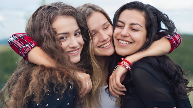 Drei Schülerinnen der Sardis Secondary School umarmen sich lachend im Freien.
