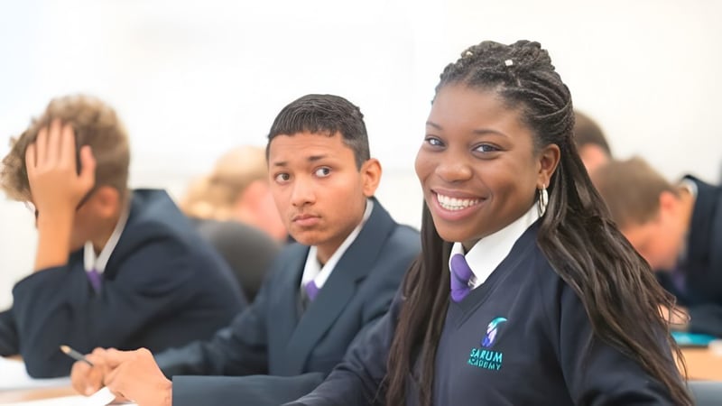 Eine Gruppe Schülerinnen und Schüler in Schuluniformen auf dem Campus der Sarum Academy, vorne eine lächelnde junge Frau.