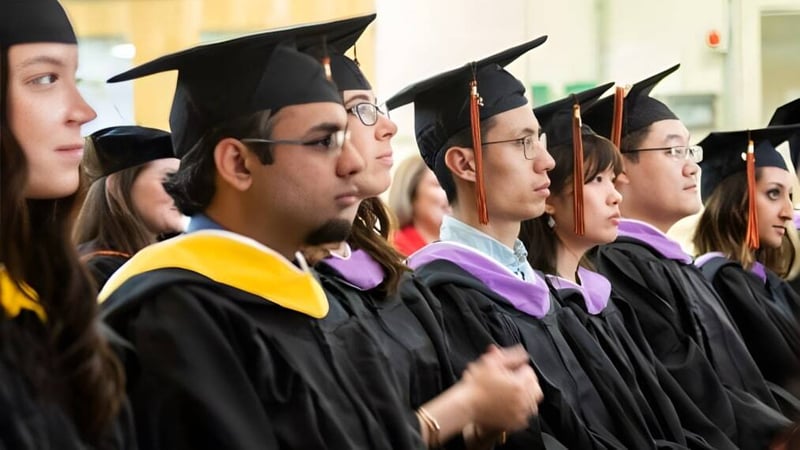 Eine Gruppe von Absolventen der Saunders Secondary School steht in akademischer Kleidung während der Abschlussfeier zusammen.