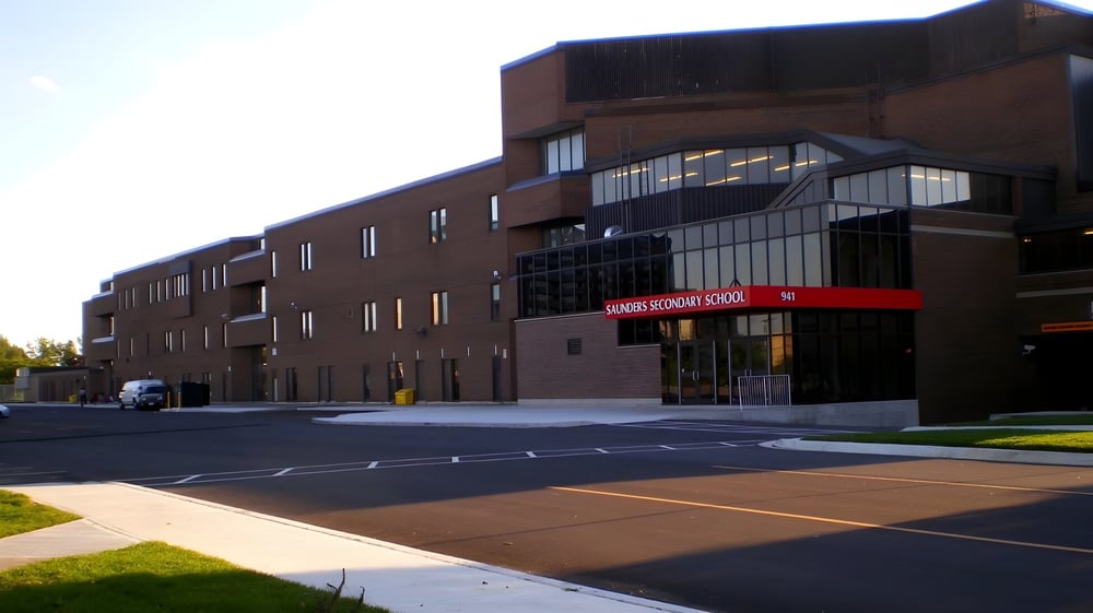Das mehrstöckige Backsteingebäude mit moderner Architektur auf dem Campus der Saunders Secondary School ist von einem Parkplatz und Grünflächen umgeben.