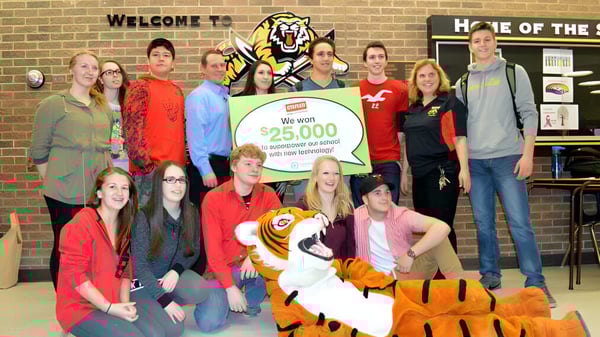 Schüler und Erwachsene der Saunders Secondary School übergeben einen großen Scheck über 25.000 US-Dollar bei einer Feierstunde.