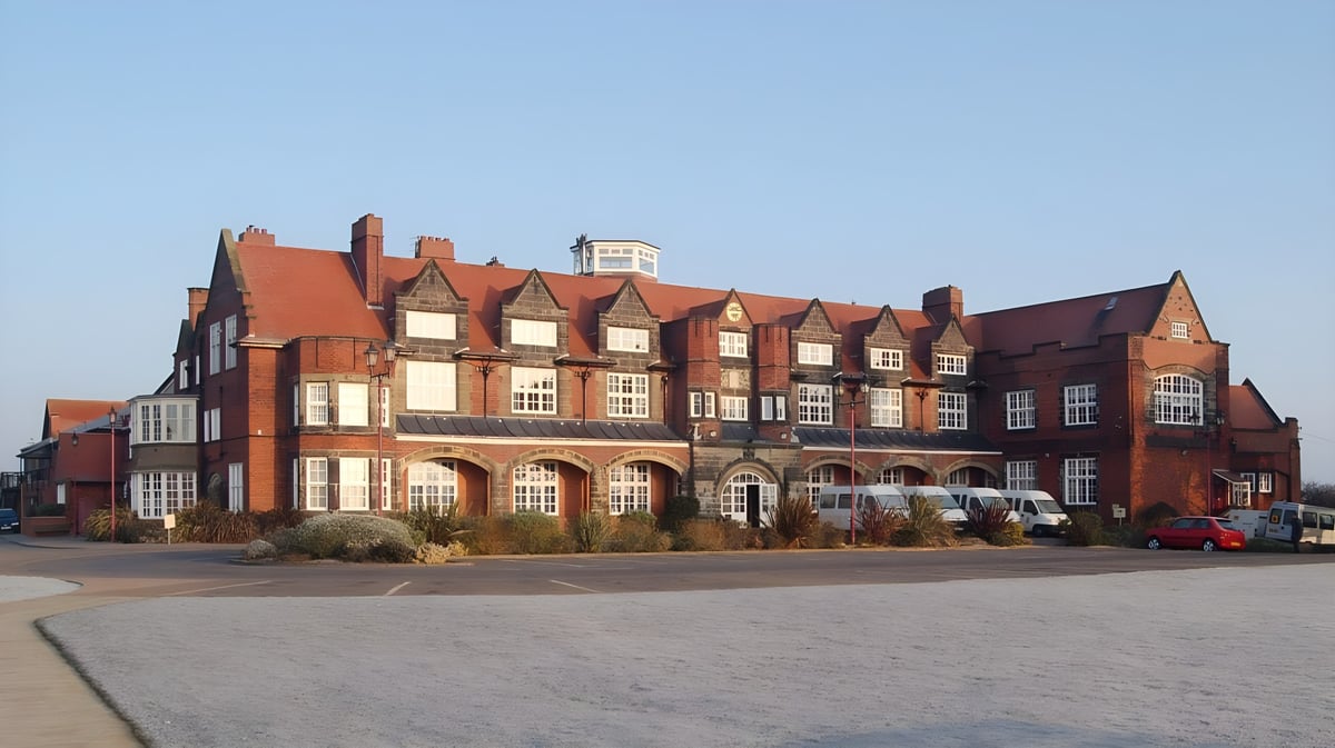Das große Ziegelgebäude mit rotem Dach und vielen Fenstern am Scarborough College steht vor einem gepflasterten Bereich mit geparkten Autos.