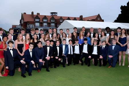 Eine große Gruppe von Schülern des Scarborough College steht auf einer Wiese vor einem historischen Gebäude mit roten Ziegeldächern.