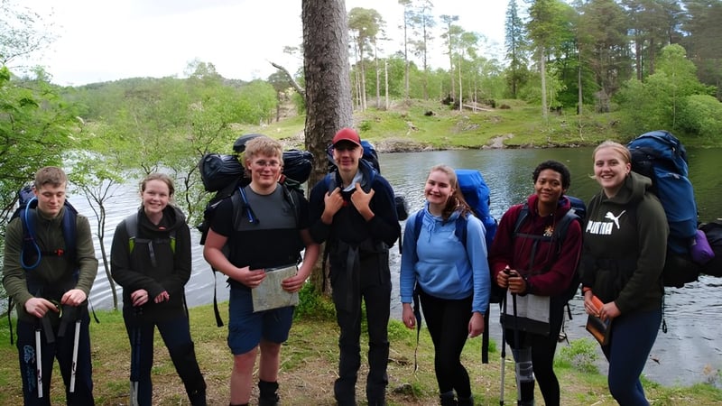 Schüler des Scarborough College stehen gemeinsam in einem bewaldeten Gebiet nahe eines Gewässers.