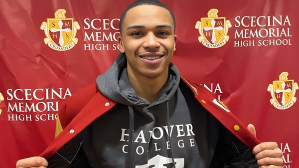 Ein Schüler steht vor dem Logo der Scecina Memorial High School vor einem roten Hintergrund.