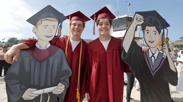 Drei Schüler in Abschlusskleidung posieren gemeinsam vor einer Wand mit Cartoon-Figuren am Schull Community College.