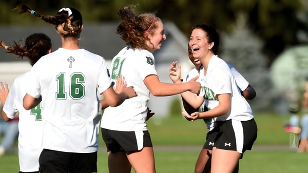 Schüler der Scoil Aireagail feiern gemeinsam auf dem Sportfeld mit Bäumen und hellem Himmel im Hintergrund.