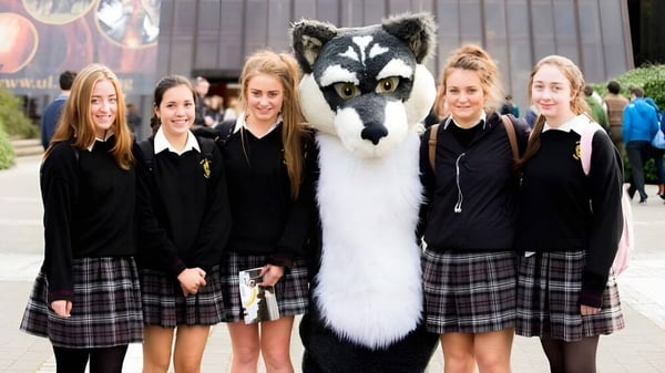 Schülerinnen der Scoil Aireagail stehen zusammen mit einem großen weißen und grauen wolfartigen Tier im Vordergrund.