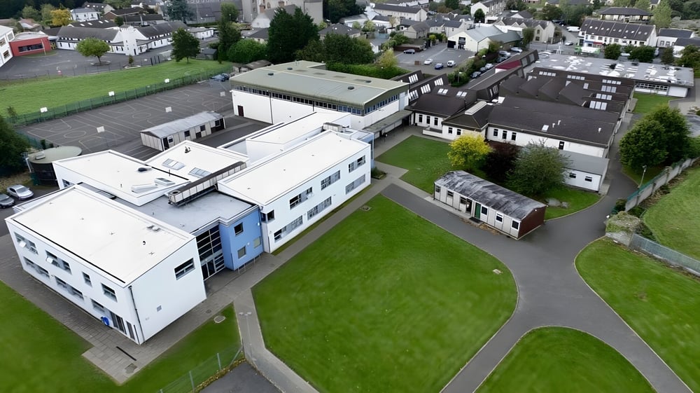Der weitläufige Campus der Scoil Dara mit moderner und traditioneller Architektur inmitten grüner Wiesen und Bäume in einer malerischen Stadt.