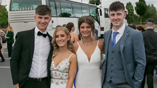 Vier Schülerinnen und Schüler der Scoil Dara stehen vor einem Bus und posieren für ein Gruppenfoto in formeller Kleidung.