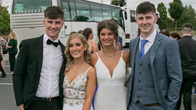 Eine Gruppe von vier jungen Erwachsenen in formeller Kleidung posiert vor einem Bus auf dem Campus der Scoil Dara.