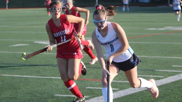 Zwei Schülerinnen der Scoil Mhuire Cork spielen nachts ein Hockeyspiel auf dem Spielfeld.
