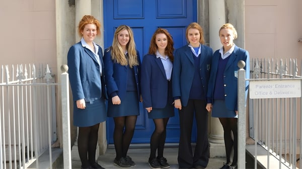 Fünf Schülerinnen der Scoil Mhuire Cork stehen in blauen Uniformen vor einer leuchtend blauen Tür.