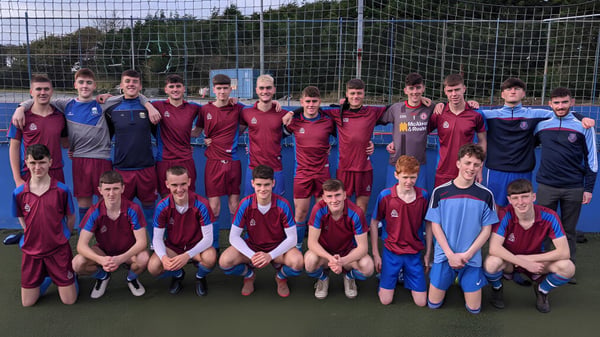 Eine Gruppe männlicher Fußballspieler posiert auf dem Spielfeld der Scoil Mhuire gan Smál in roten und blauen Trikots.