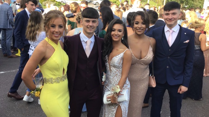 Eine Gruppe gut gekleideter Personen posiert zusammen an einem grünen Platz auf dem Campus der Scoil Mhuire gan Smál.