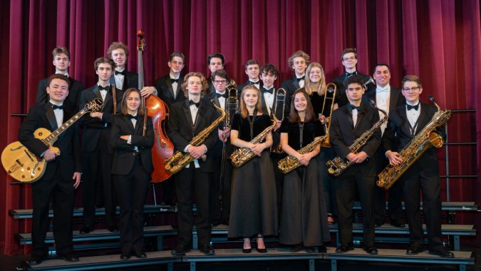 Eine Gruppe von Schülern der Scoil Mhuire gan Smál spielt auf einer Bühne vor rotem Vorhang verschiedene Musikinstrumente.