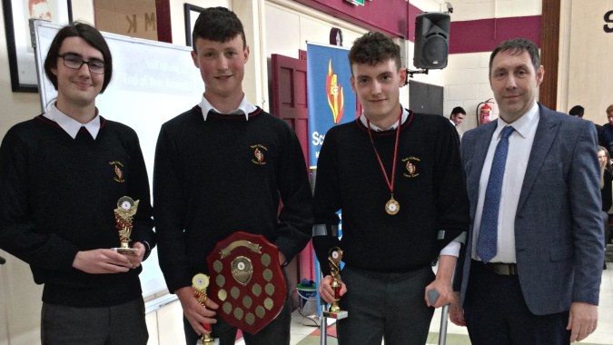 Vier Schüler in Schuluniformen von Scoil Mhuire Kanturk halten gemeinsam im Schulgebäude ihre Trophäen.