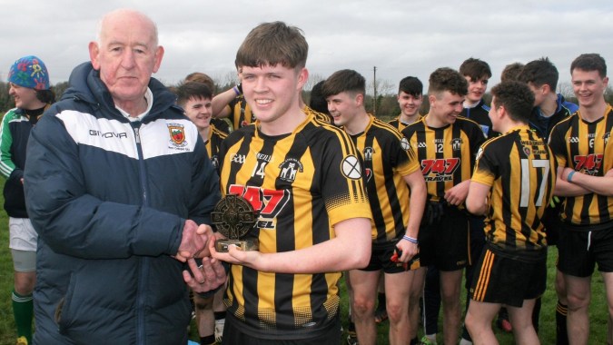 Eine Gruppe junger Fußballspieler posiert mit ihrem Trainer auf dem Sportplatz der Scoil Mhuire (Strokestown).