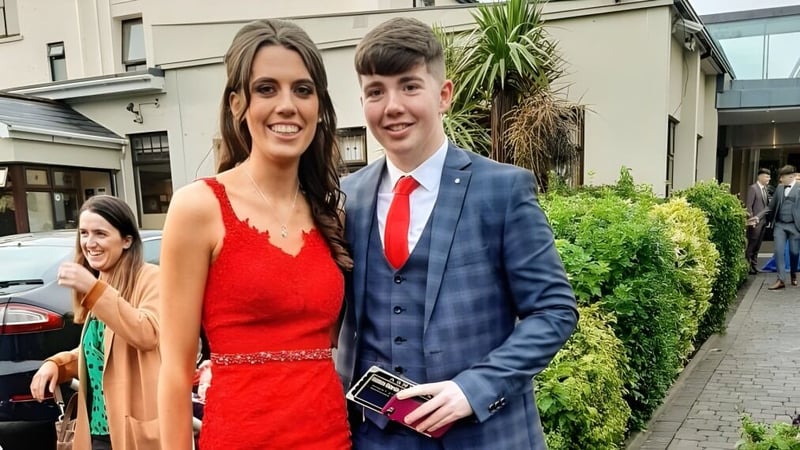 Ein junges Paar steht vor einem Gebäude mit Grünpflanzen auf dem Gelände der Scoil Mhuire (Strokestown).