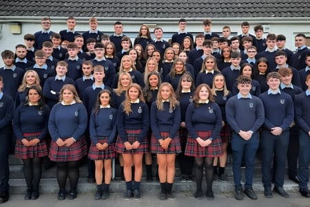 Eine Gruppe von Schülerinnen und Schülern in Schuluniform steht vor einem Gebäude mit Ziegeldach auf dem Campus der Scoil Mhuire (Strokestown).