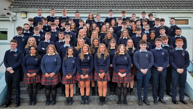 Eine Gruppe Schüler in dunkelblauer Schuluniform steht vor einem Gebäude mit Ziegeldach auf dem Campus der Scoil Mhuire (Strokestown).