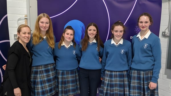 Eine Gruppe Schülerinnen der Scoil Mhuire (Trim) steht vor einem lila Hintergrund mit abstrakten Mustern.