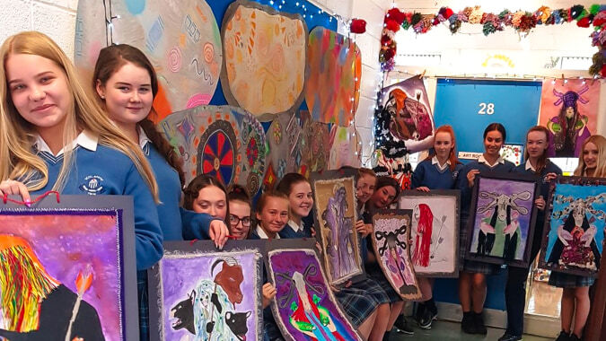 Schüler der Scoil Mhuire (Trim) stehen vor einem bunten Wandbild im Klassenraum mit verschiedenen Kunstwerken.