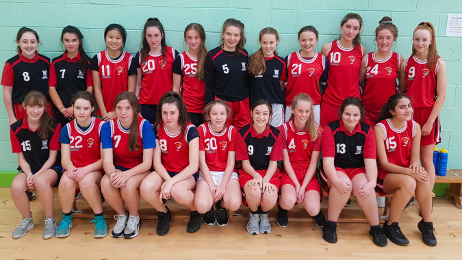 Eine Gruppe junger Sportlerinnen in roten und schwarzen Uniformen posiert in einer Sporthalle der Scoil Mhuire (Trim).