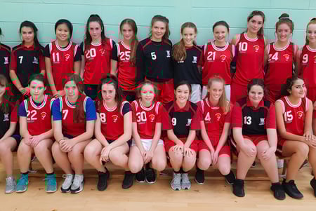 Eine Gruppe junger Volleyballspielerinnen in roten und schwarzen Trikots auf dem Spielfeld der Scoil Mhuire (Trim).