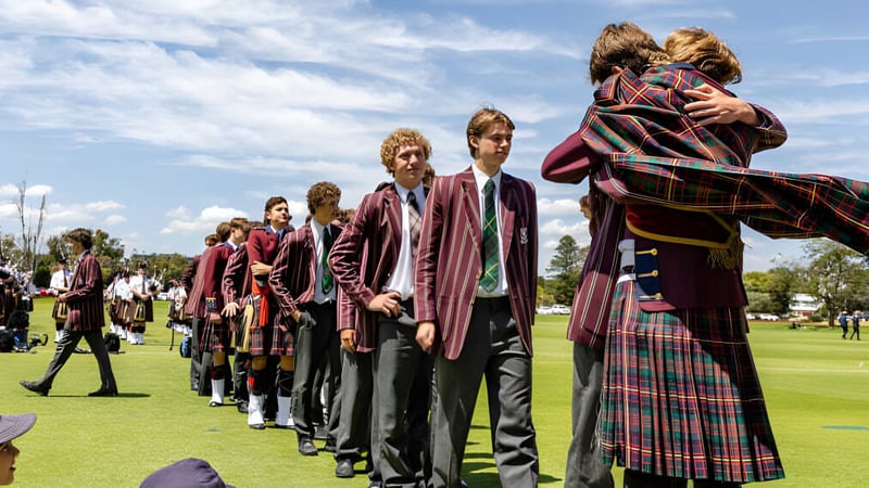 Eine Gruppe von Schülern des Scotch College steht in farbenfrohen Kilts auf einem grasbewachsenen Feld unter blauem Himmel.