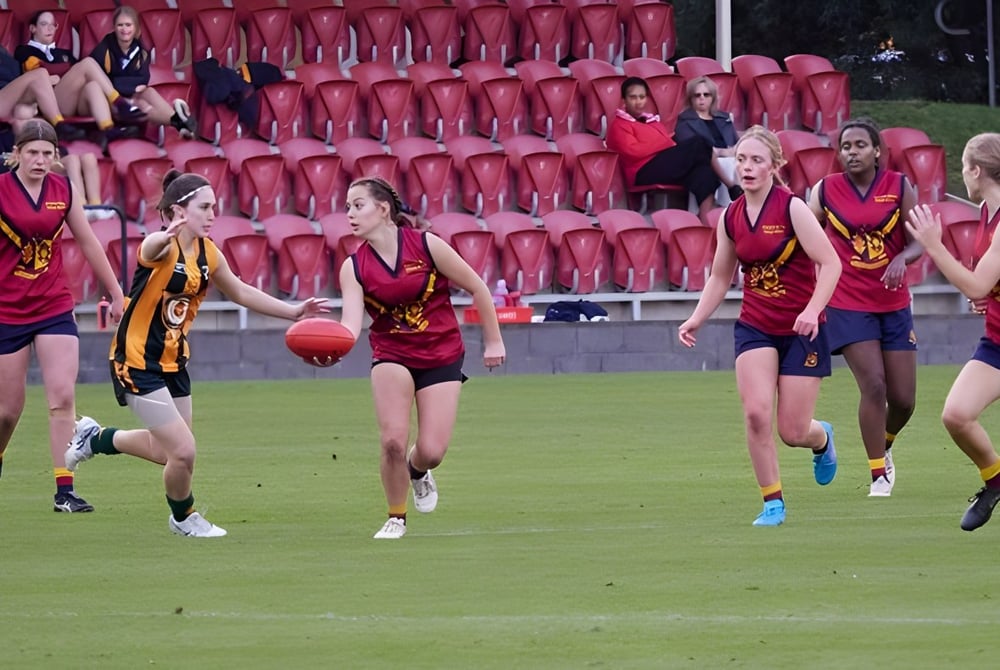 Eine Gruppe junger Sportlerinnen spielt auf dem Sportfeld des Scotch Oakburn College vor Zuschauern.