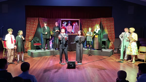 Auf der Bühne des Scots College sind Schaufensterpuppen mit bunten, vintage-inspirierten Kostümen vor gemusterten Vorhängen und Kunstwerken zu sehen.