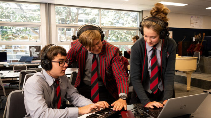 Schüler des Scots College lernen gemeinsam an einem Laptop in einem Klassenraum mit großen Fenstern.