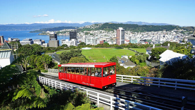 Eine rote Seilbahn fährt über eine grüne Landschaft mit Stadt und Bergen im Hintergrund auf dem Gelände des Scots College.