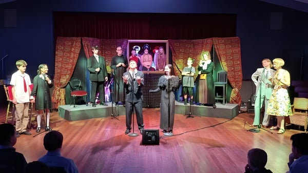 Auf der Bühne des Scots College sind Schaufensterpuppen mit bunten, vintage-inspirierten Kleidern vor einem gemusterten Vorhang und Kunstwerken zu sehen.